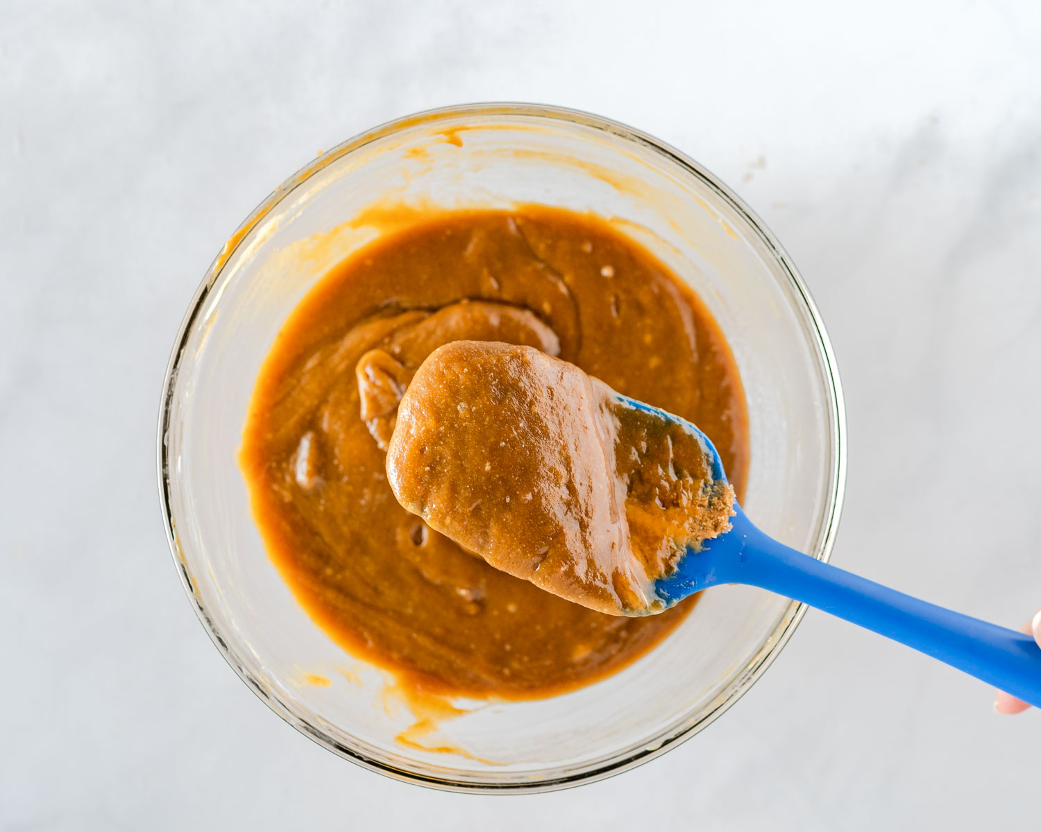 A bowl of a peanut butter mixture with a spatula sitting over it showing how thick the mixture is.