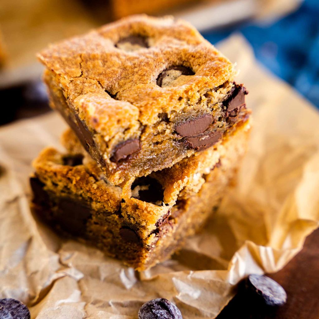 Side view of cut peanut butter brownie bars stacked on a piece of parchment paper and surrounded by chocolate chips.