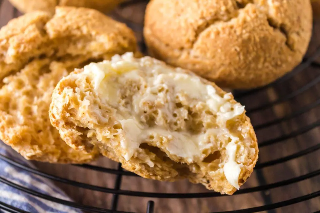 A buttered baked roll sitting in front of a whole roll.