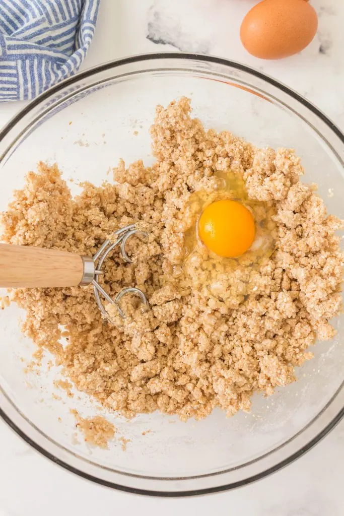 A bowl filled with a mixture of Matzo and water with a raw egg being mixed in.