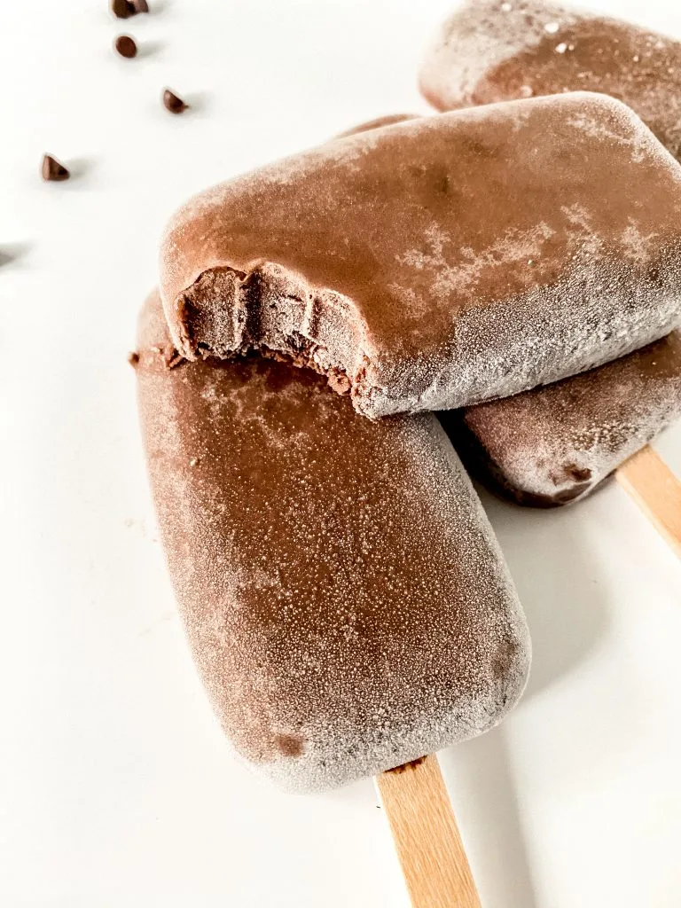 A frozen chocolate popsicle with a bite taken out of it.