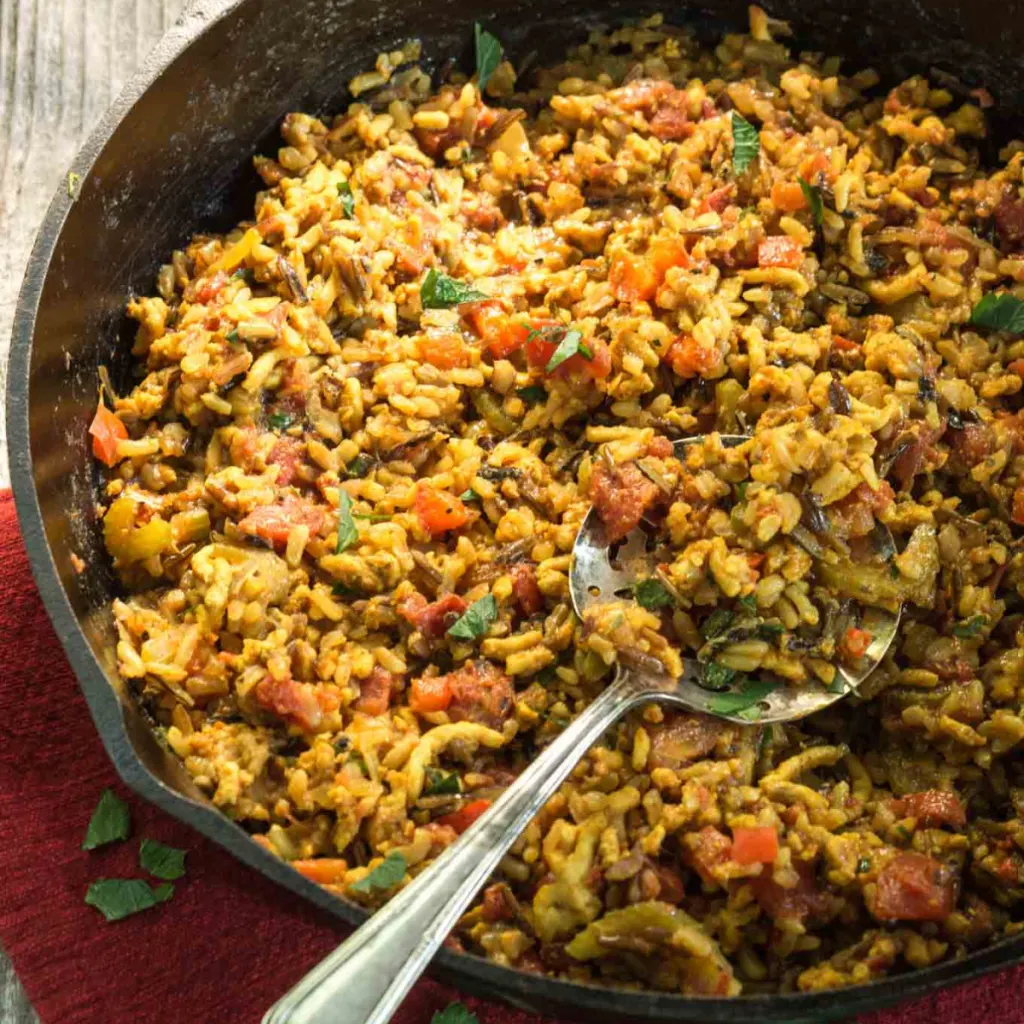 3/4 view of a spoon over a skillet filled with rice, ground chicken, tomatoes, and parsley.