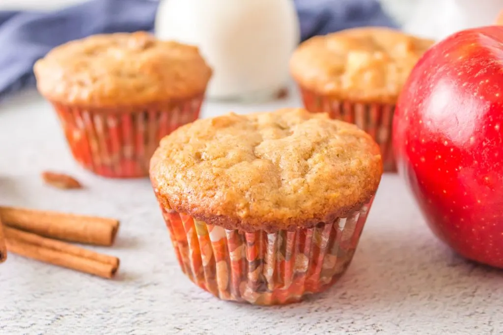 Single apple cinnamon muffin in focus, close-up, horizontal image with other muffins blurry in the background.