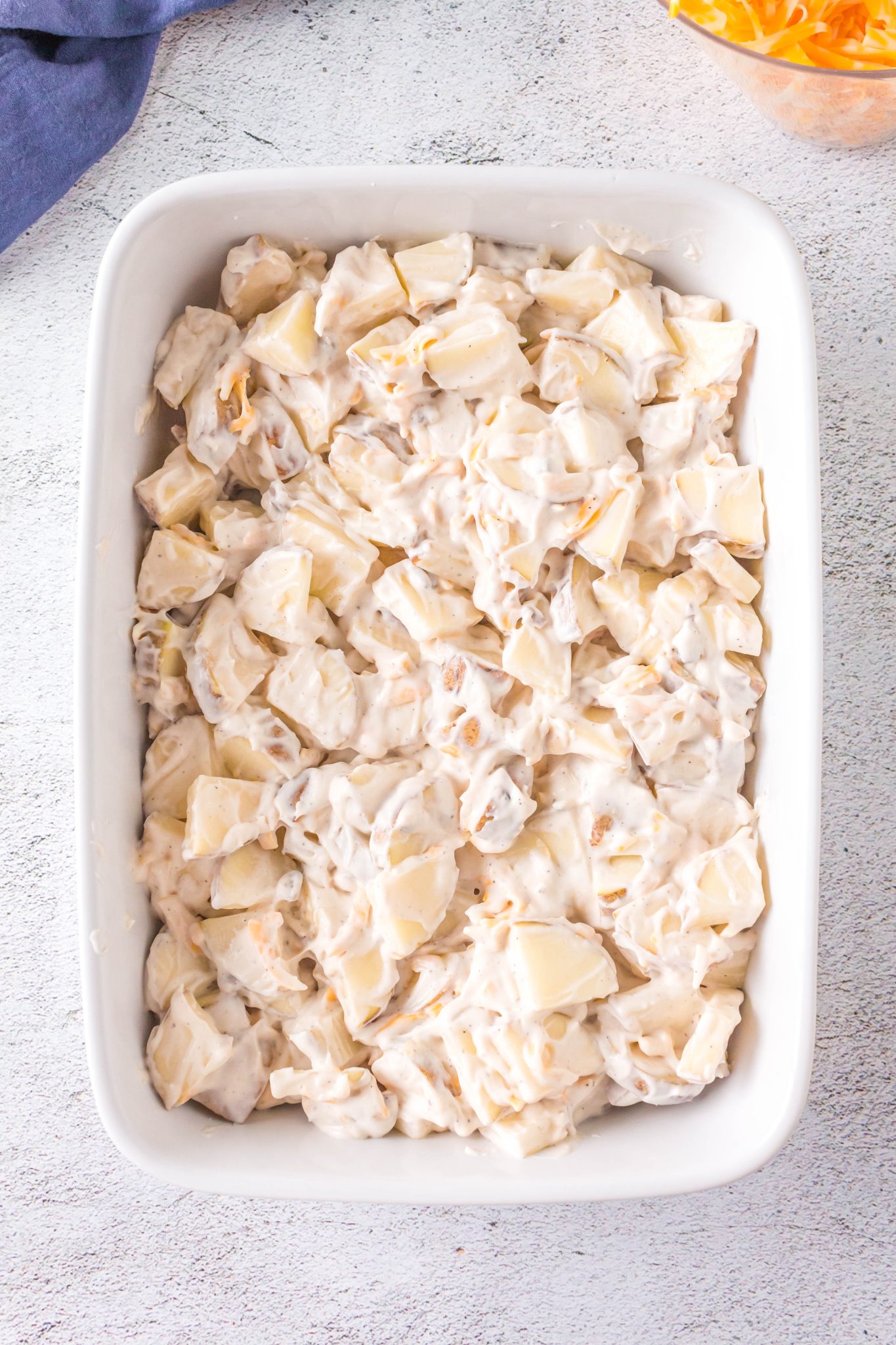 Top down view of a potato casserole loade with diced potatoes and cheese in a creamy sauce ready to go into the oven.