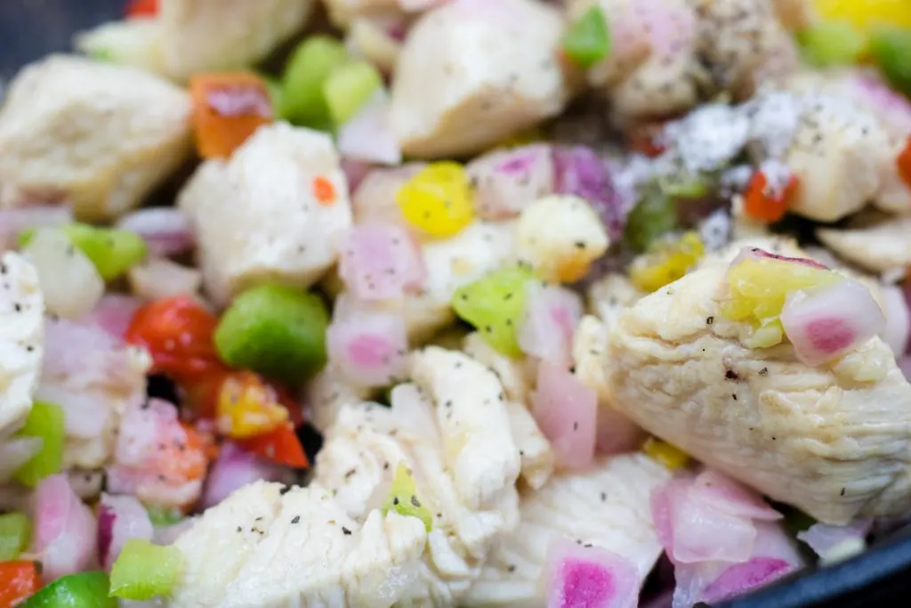 chicken, onions and bell peppers cooking in a skillet.