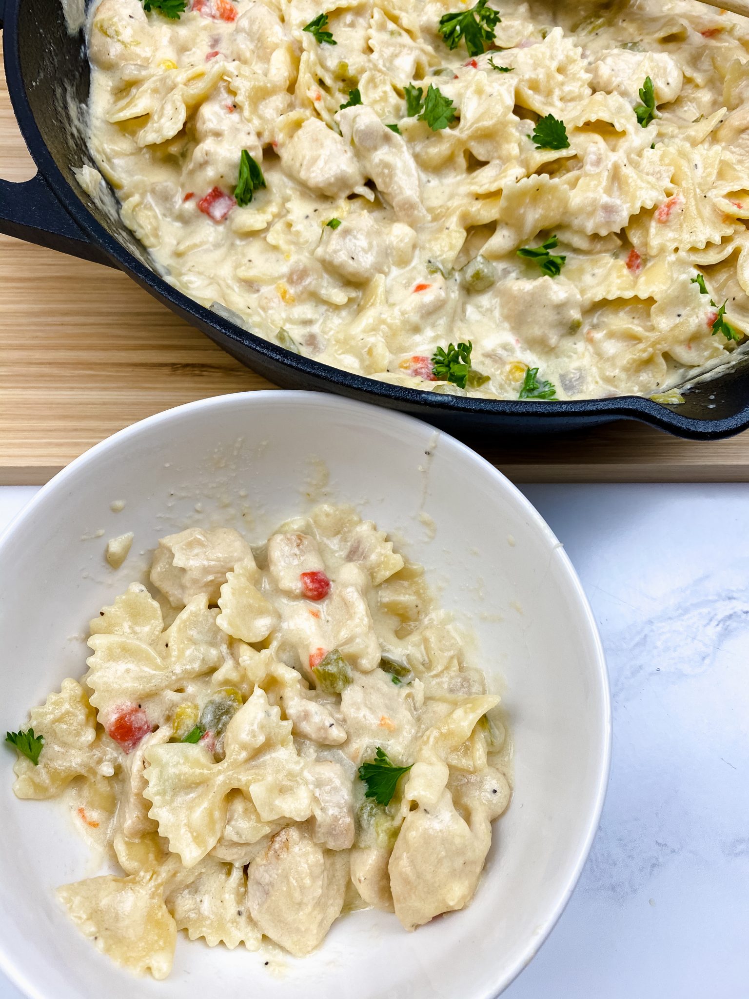 Cast iron skillet filled with garlic parmesan chicken pasta. Single serving in a white bowl.