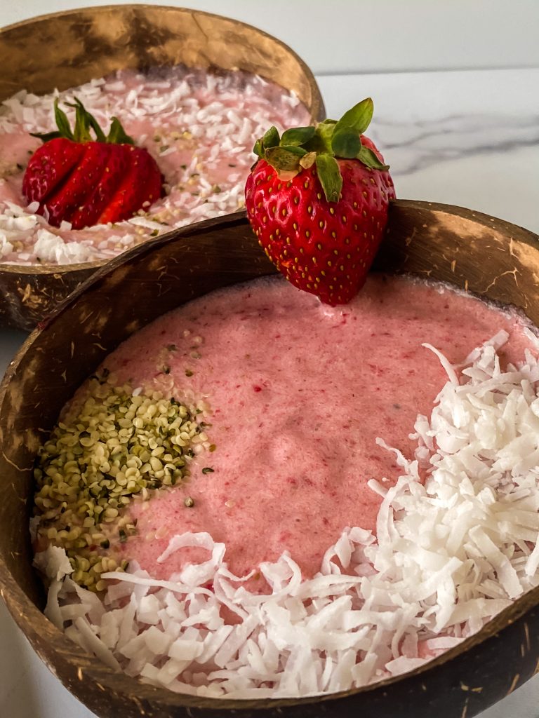 Strawberry Banana Smoothie bowls in wooden bowls topped with coconut flakes and a strawberry sitting on a marble countertop.