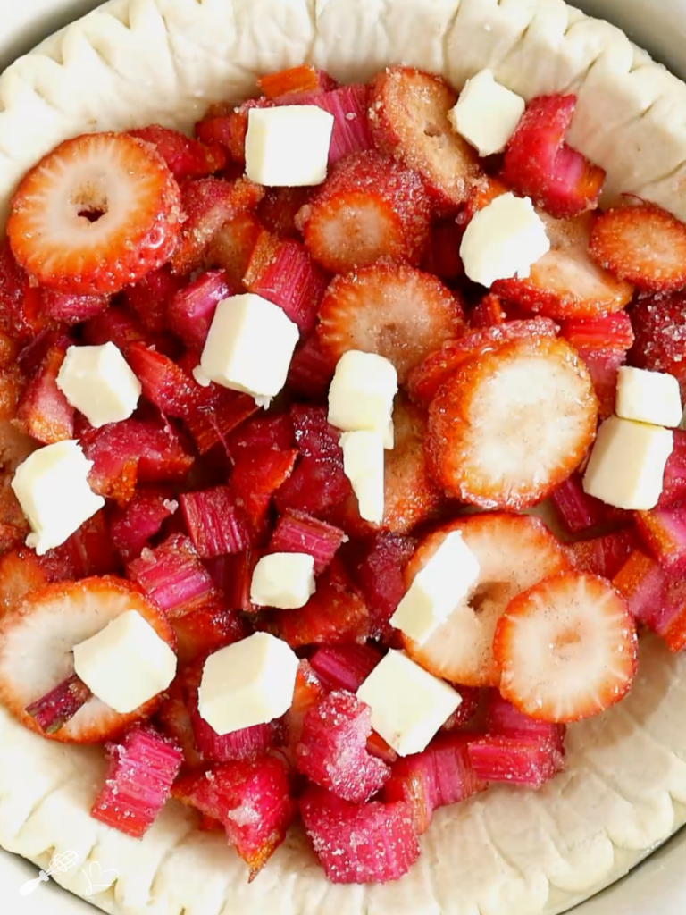 Strawberries and rhubarb filling in a pie crust dotted with pieces of butter.