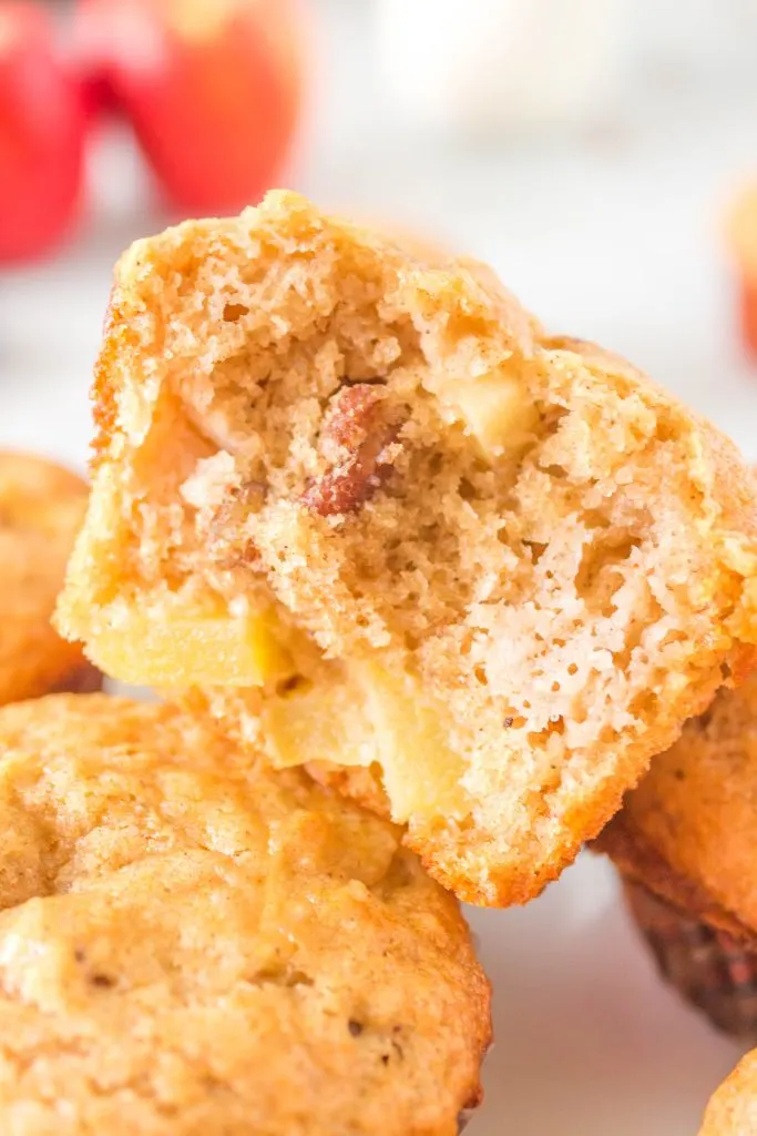 A muffin torn in half showing pecans and pieces of apple.