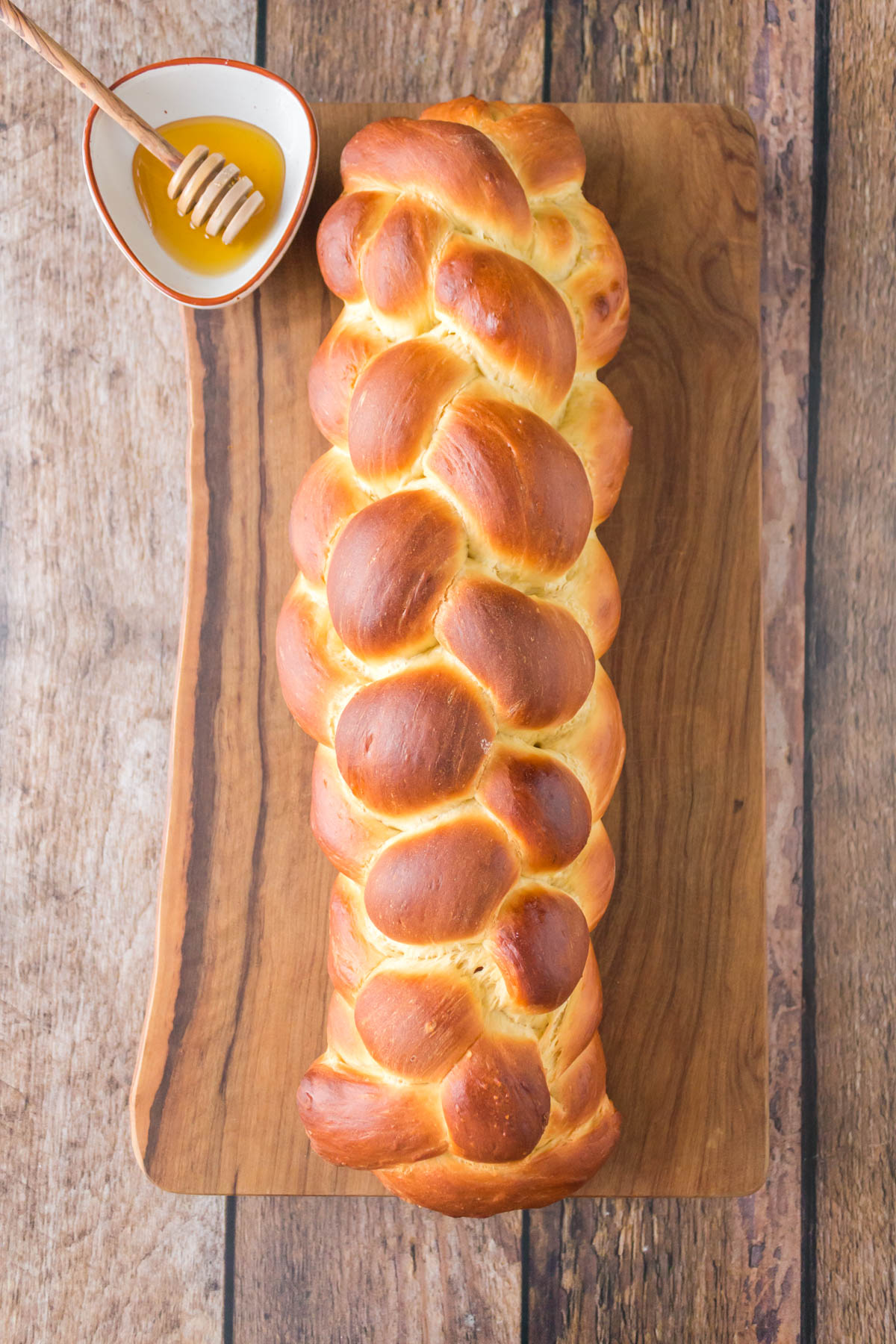 Top down view of a loaf of 6-strand braided Challah bread sitting next to a bowl of honey - Hostess At Heart.