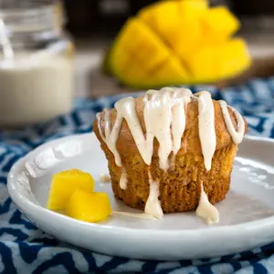 Side view of a muffin with vanilla glaze on a plate with mangos