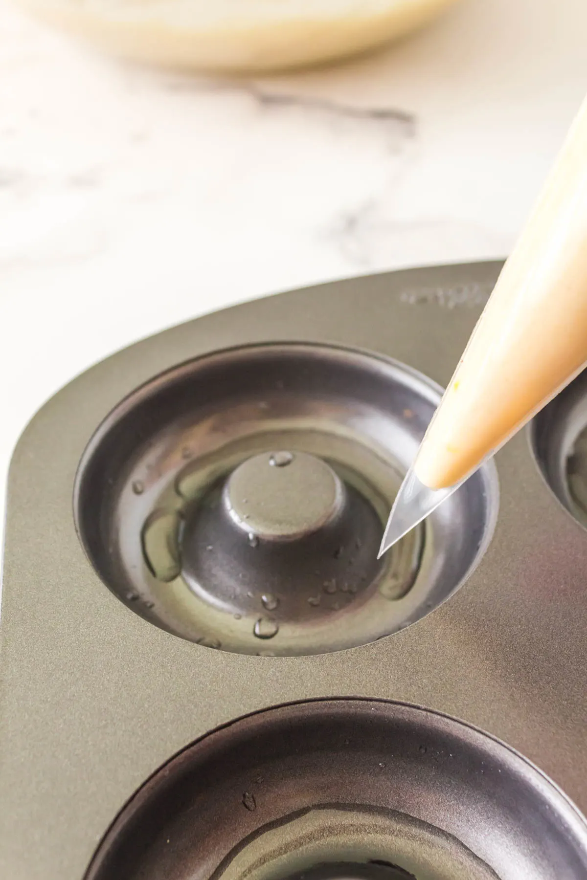 A piping bag filled with doughnut batter hovering over a doughnut pan