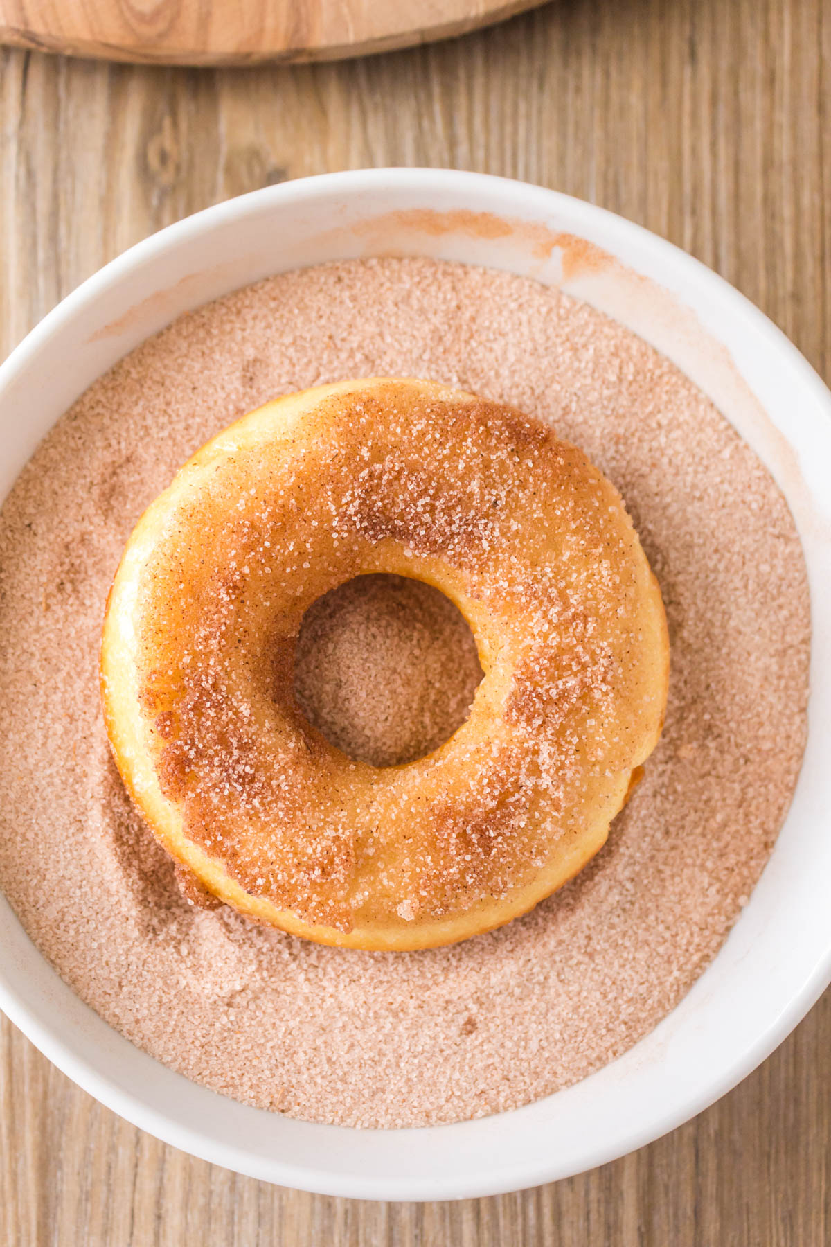 A doughnut sitting in a bowl of cinnamon and sugar mix.