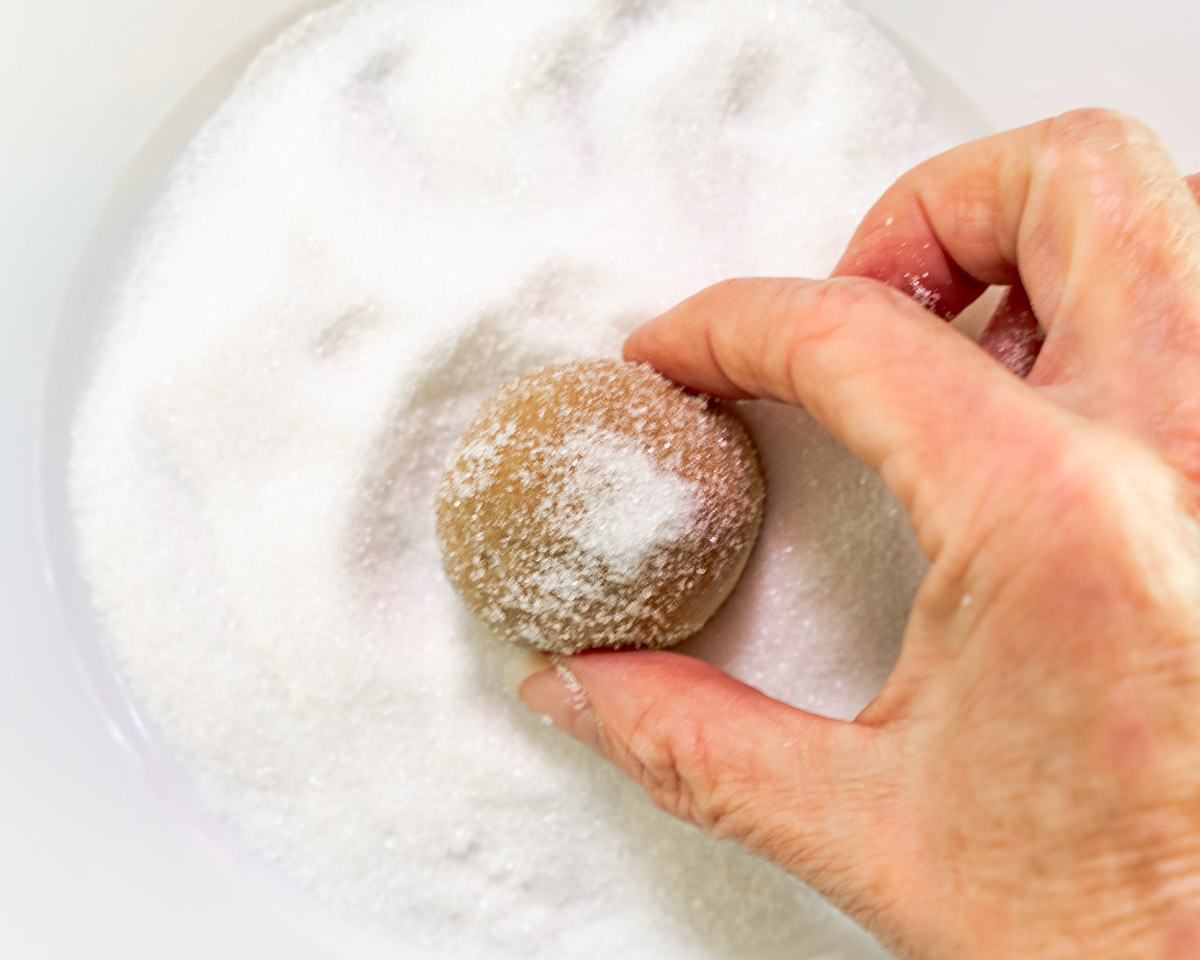 A ball of peanut butter dough being rolled in sugar.
