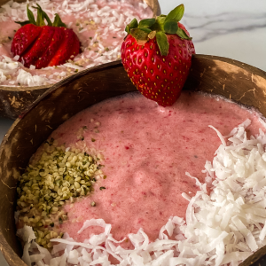 Angled view of a bowl filled with strawberry smoothie topped with seeds and coconut.