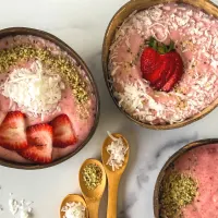 Top down view of three bowls of Strawberry smoothy bowls topped with seeds and coconut.