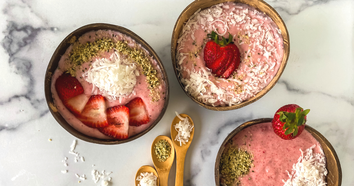 Top down view of three bowls of Strawberry smoothy bowls topped with seeds and coconut.