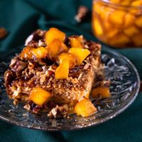 An angled photo of a serving of Homemade Peach Cobbler topped with peach bourbon sauce.