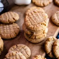 Angled view of peanut butter cookies with fork marks on a cutting board.