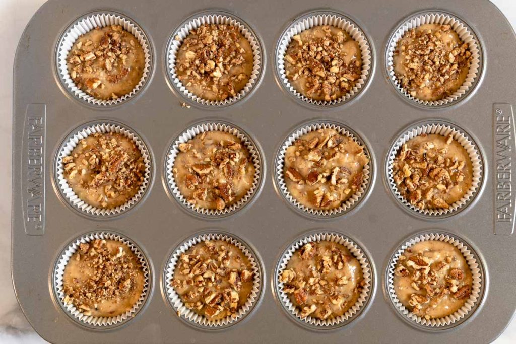 A muffin tin filled with banana muffins topped with ground nuts.