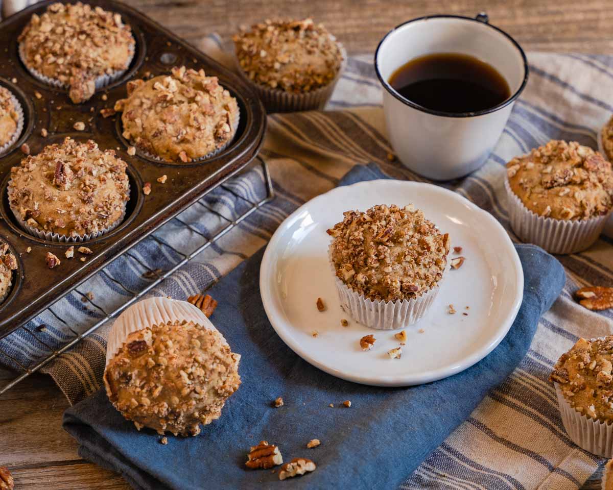 3/4 view of a bananna muffin sitting on a plate surrounded by more homemade banana muffins