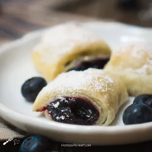 Blueberry Puff Pastry Dessert Rolls sitting on a plate dusted in powdered sugar.