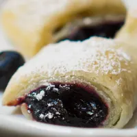 Blueberry puff rolls sitting on a plate with fresh blueberries