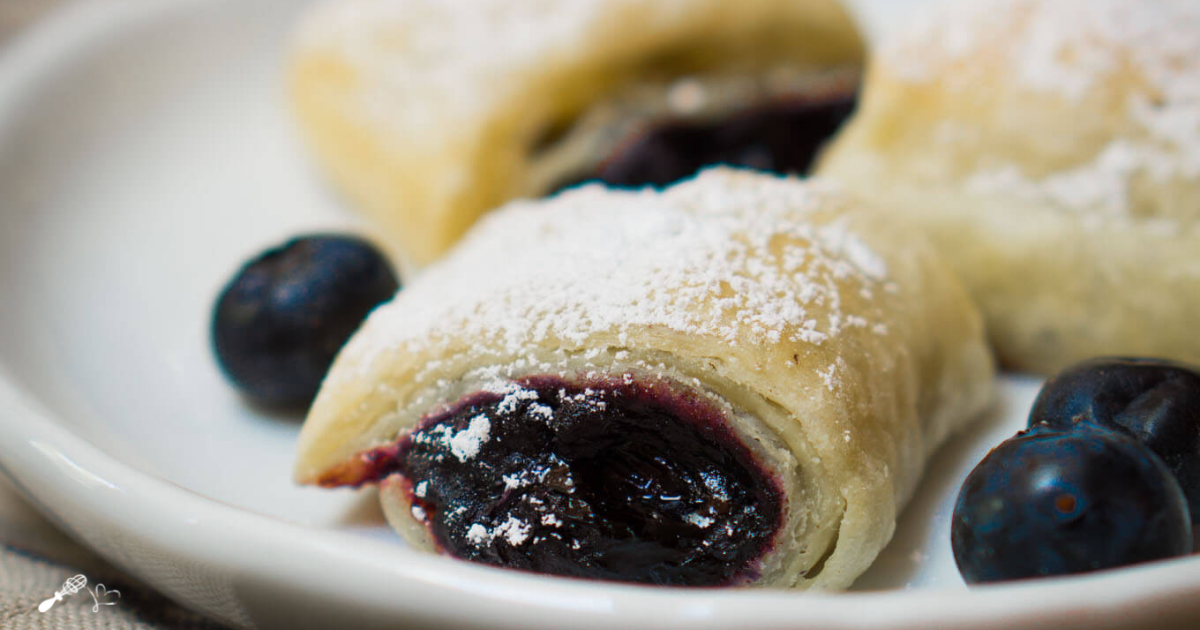 Blueberry puff rolls sitting on a plate with fresh blueberries