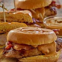 Close up view of a chicken sandwich topped with bacon and sauce.
