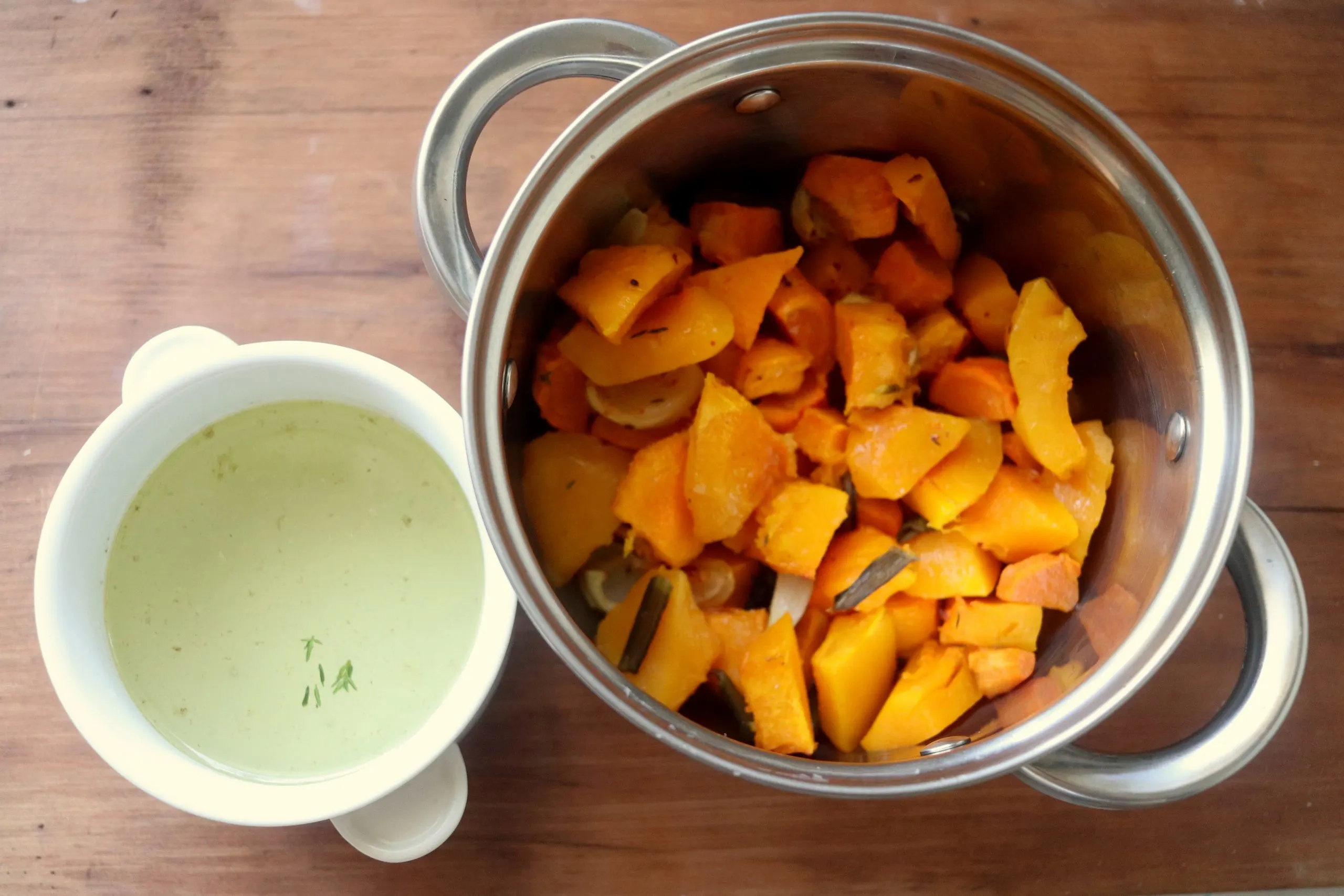 Top down photo of roasted squash and vegetables in a saucepan with a cup of broth on the side.