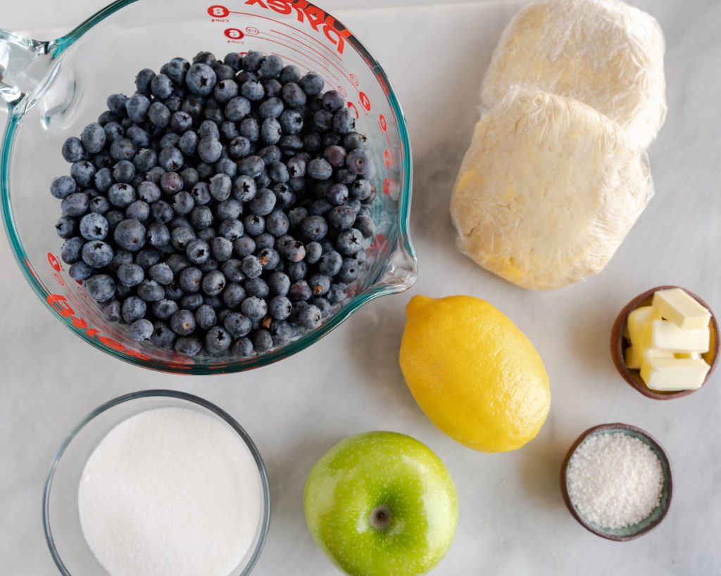 Ingredients for the blueberry pie recipe: blueberries, pie crust, sugar, tapioca powder, shredded apple, butter, salt, lemon.