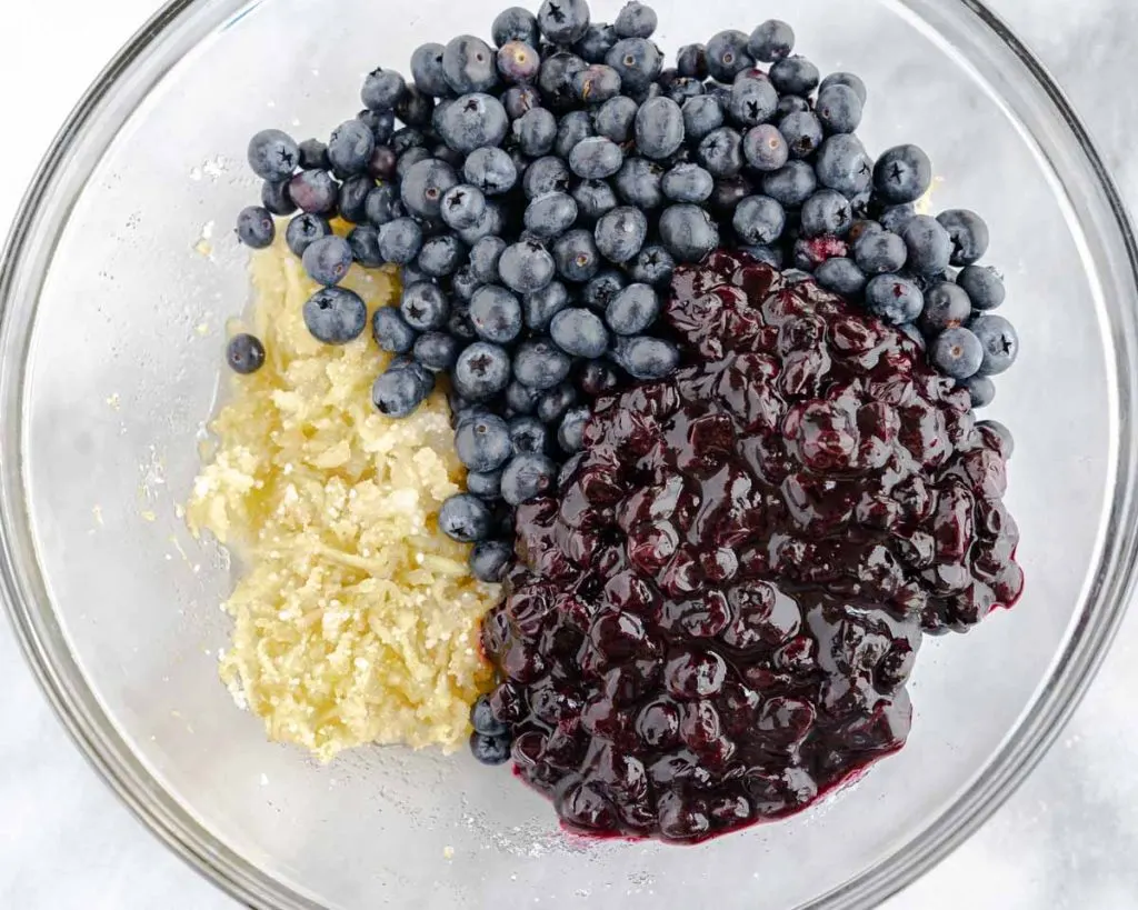 Frozen and cooked blueberries on the top of a mixing bowl filled with other pie filling ingredients.