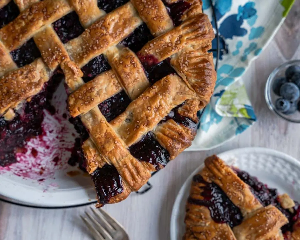 Close up top down view of a homemade blueberry pie plus one slice removed. 