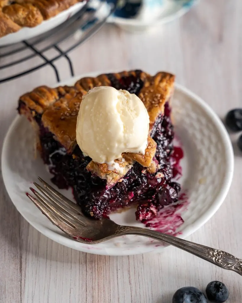 Close-up view of a single slice of pie in focus with a scoop of ice cream on top.