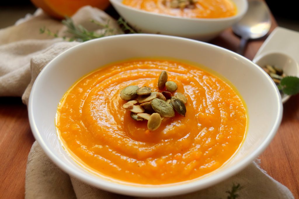 A bowl filled with soup made from squash topped wit pepita seeds.