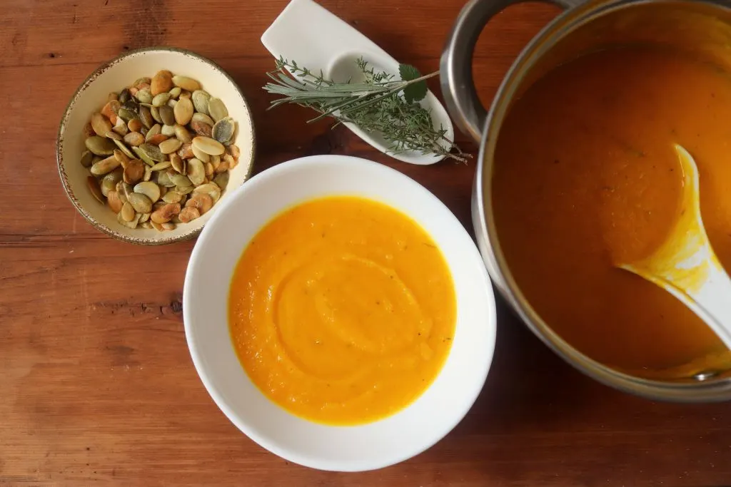 A bowl of squash soup sitting next to a dish of pumpkin seeds.