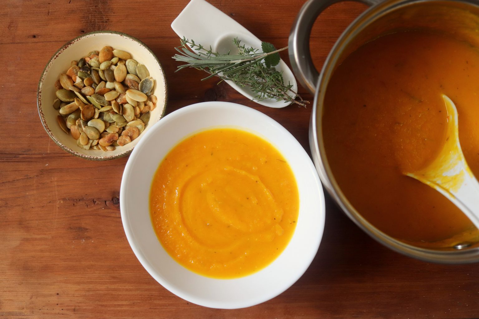 A bowl of squash soup sitting next to a dish of pumpkin seeds.