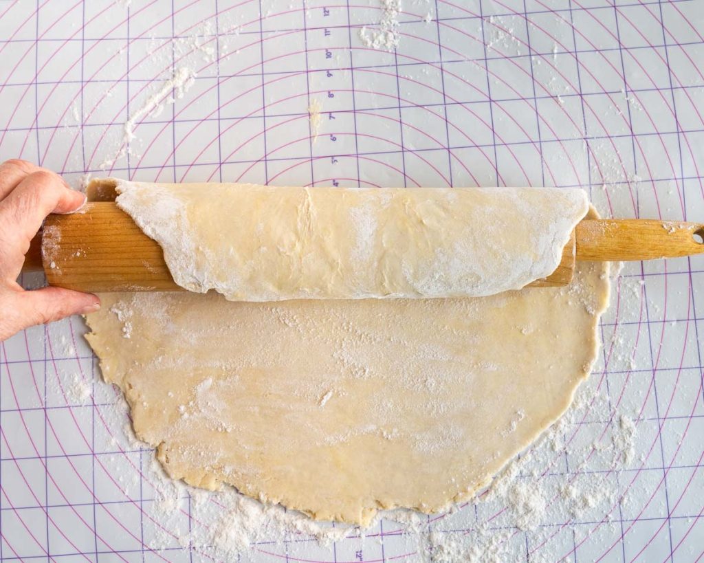 Picking up rolled pie crust made with butter using a rolling pin.