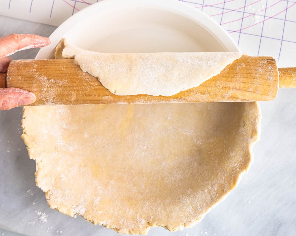 Placing a rolled pie crust into a pie plate using a rolling pin.