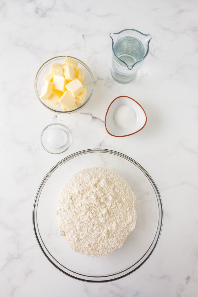 Ingredients used to make a butter pie crust including water, sugar, salt, flour, and butter.