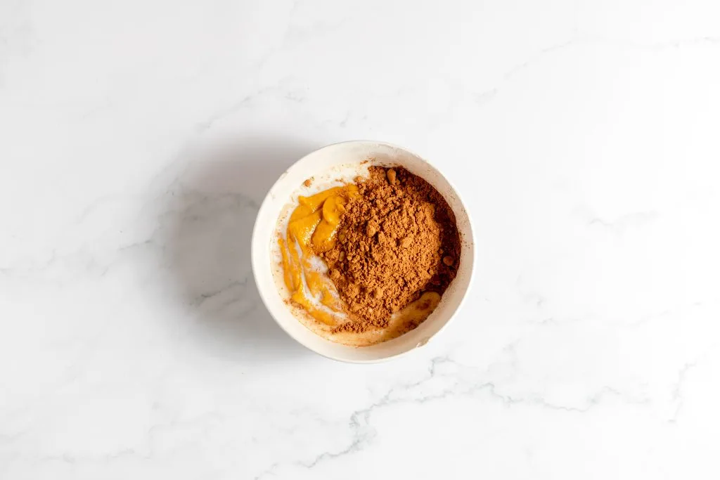 Chocolate cocoa added to pumpkin batter in a bowl