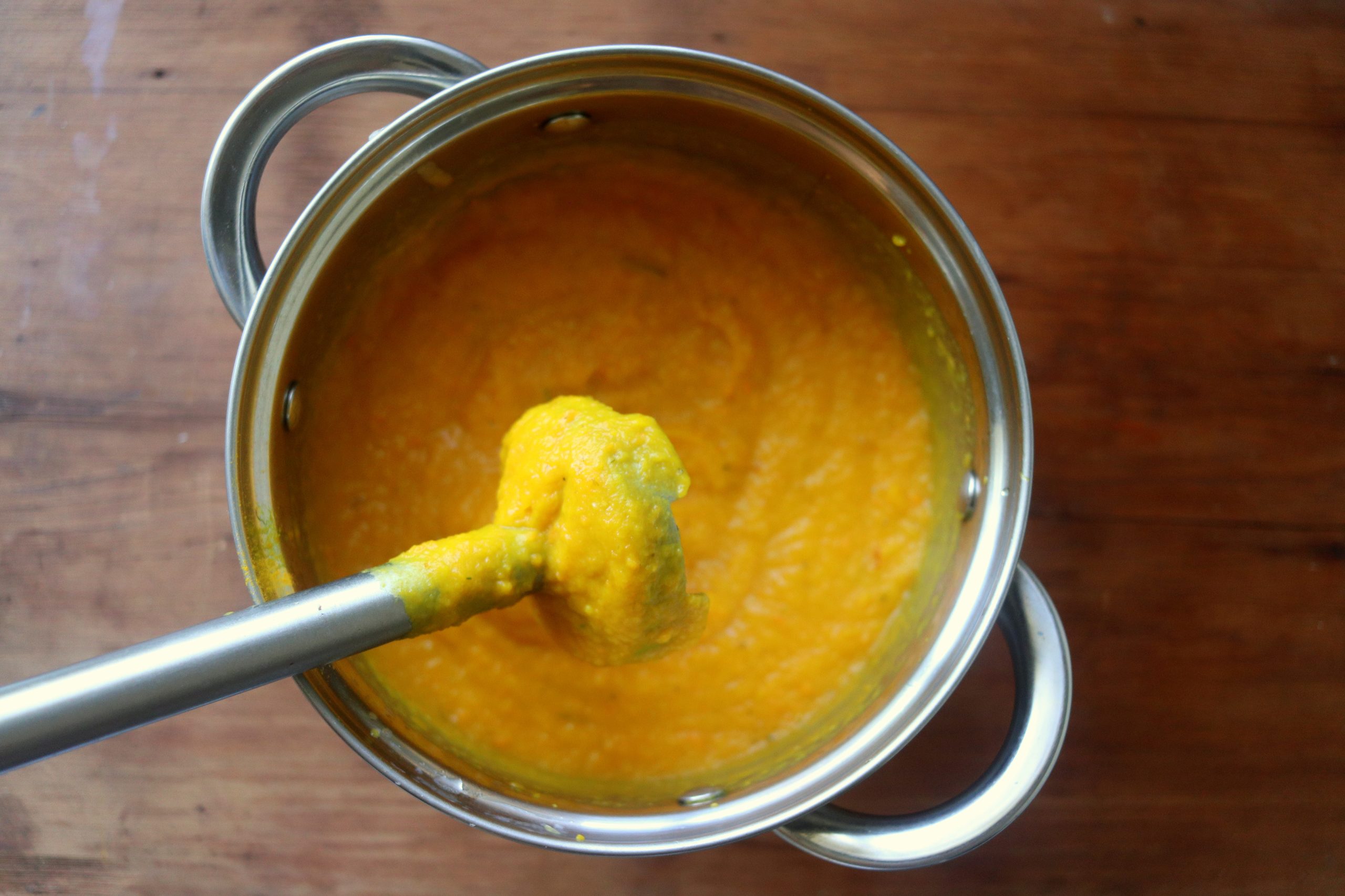 A saucepan filled with vegetable puree with an immersion blender