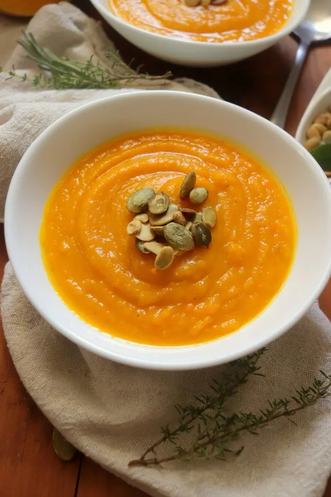 Close up view of a bowl filled with soup made from squash and garnished with pumpkin seeds.