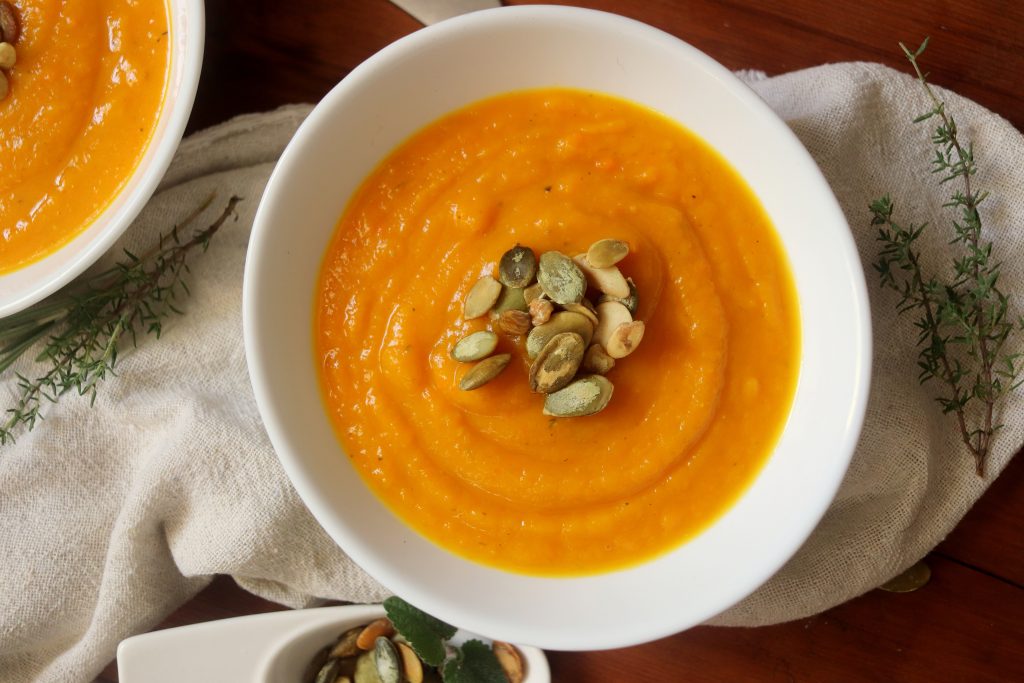 Top down view of a bowl of creamy squash soup topped with pepita seeds.