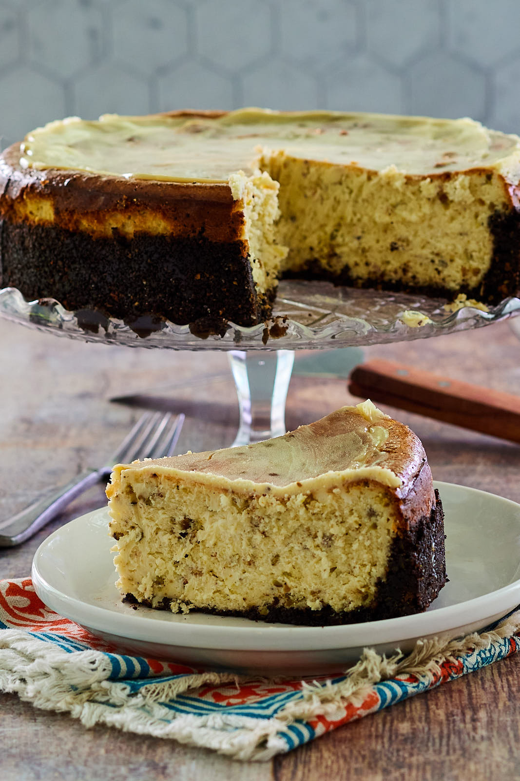 Full White Chocolate Pistachio Cheesecake on a platter with a single slice removed and plated in front.