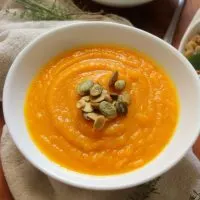 Close up view of a bowl filled with soup made from squash and garnished with pumpkin seeds.