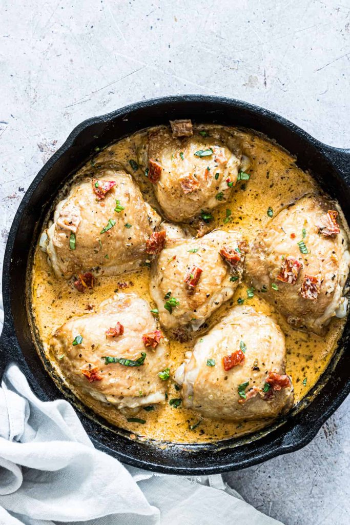 Chicken thighs sitting in a cream sauce in a cast iron skillet