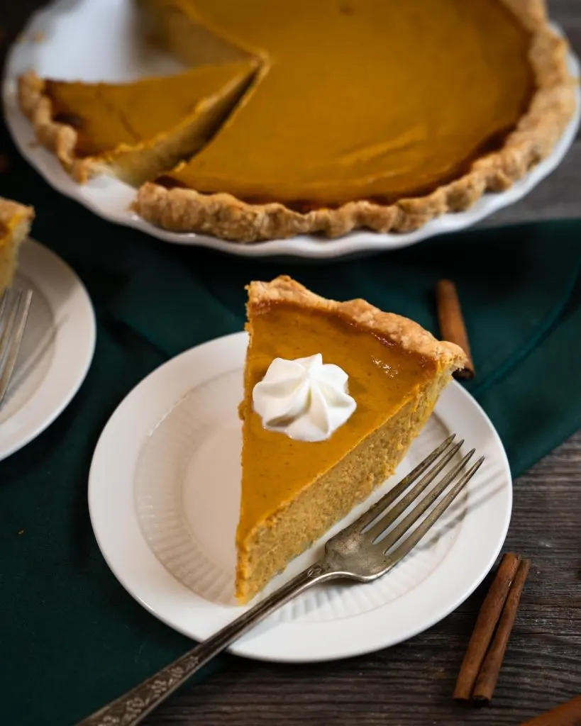 3/4 angle of a smooth and creamy slice of pumpkin pie topped with whipped topping.