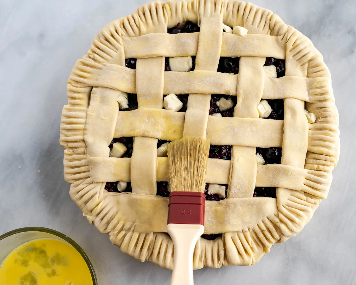 Egg wash being brushed on raw pie dough.