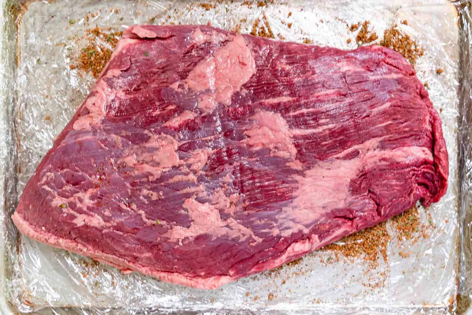A raw brisket sitting on a baking sheet dusted with dry rub ingredients.